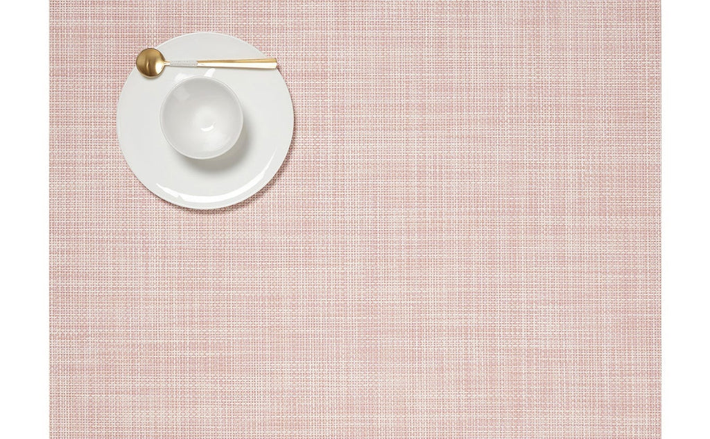 An aerial view of a rectangular, blush pink placemat made of woven vinyl