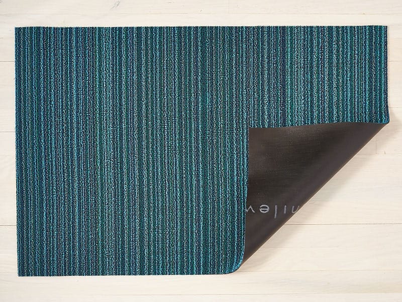 a skinny stripe design rectangular floor mat in shades of turquoise and blue, made of eco friendly looped vinyl, backed with black commercial rubber