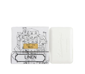 A white bar of linen scented soap next to its packaging, which features the Lothantique logo and a simple black line drawing of French-style buildings on a white background.