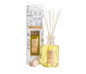 A clear, glass bottle of Clementine scented diffuser, with 7 bamboo reeds in the neck of the bottle and a beige label printed with "batons a parfum, fragrance diffuser, clementine" and the Lothantique logo. Shown with a second bottle in white packaging with black line drawings of French houses.