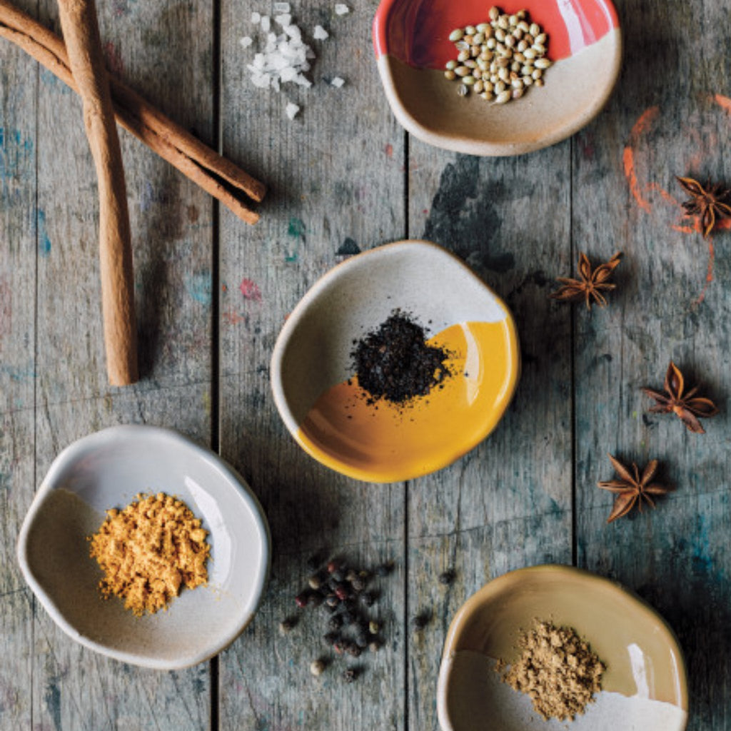 A warm, rustic table setting showing Solar pinch bowls and an array of spices