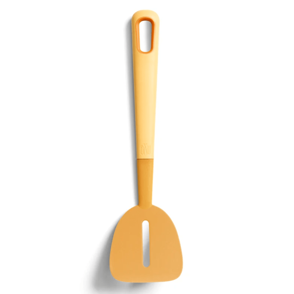 A mustard yellow slotted turner with a sleek design on a white background, featuring an angled head and a comfortable soft grip handle. Ideal for flipping and lifting food while leaving unwanted bits behind.