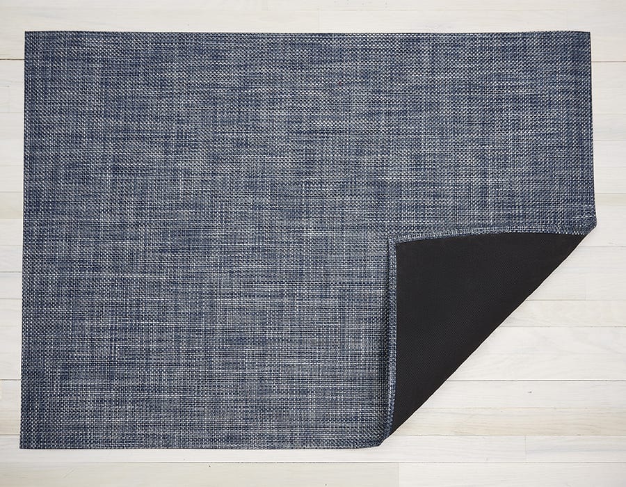 a rectangular woven floor mat made of an environmentally friendly vinyl yarn in dark blues and white, giving the look of denim
