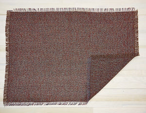 A backless, rectangular woven floor mat made of eco friendly vinyl in shades of burgundy and blue with fringes along each edge