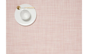 An aerial view of a rectangular, blush pink placemat made of woven vinyl