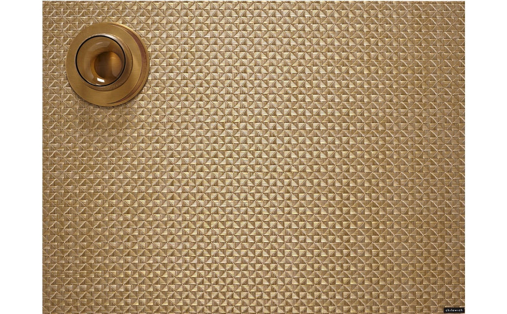 a rectangular, origami style weave placemat in metallic gold made of eco friendly vinyl