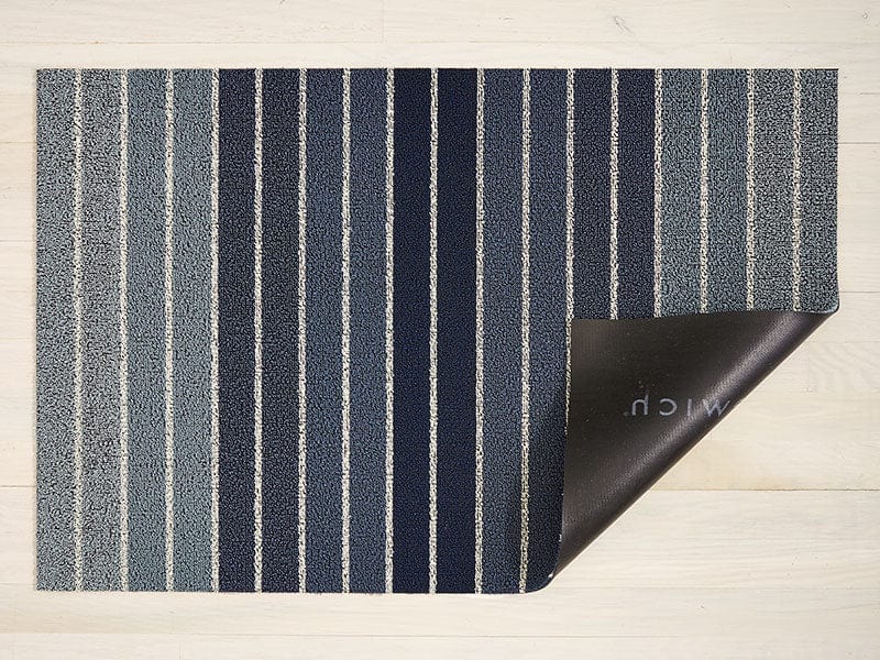 a rectangular floor mat backed with black commercial rubber made of eco friendly looped vinyl yarns with a striped design in shades of blue and white