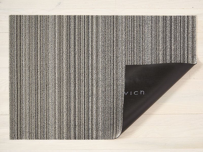 a skinny striped rectangular floor mat in the shades of a birch tree, made of eco friendly looped vinyl yarn, backed with black commercial rubber