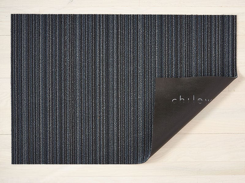a rectangular floor mat with a skinny stripe design in dark blue hues, made of eco friendly looped vinyl yarn, backed with black commercial rubber