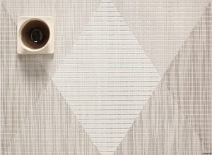 a geometric, woven, rectangular placemat in shade of off white, beige, and grey with a diamond center and triangles surrounding