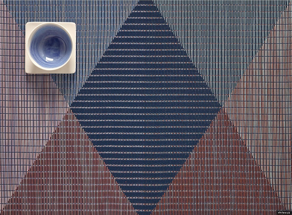 a rectangular woven placement with a modern pattern of a diamond in the center with triangles surrounding, in shades of blue and burgundy