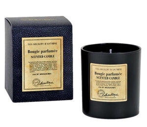 Black glass candle jar, and black box with a aged look paper label. The words Les Secrets d'Antoine bougie parfumee, scented candle printed on it with the lothantique logo at the bottom