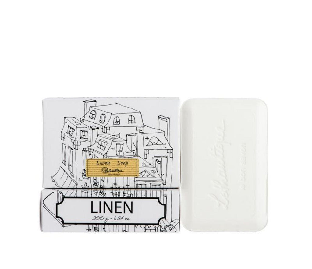 A white bar of linen scented soap next to its packaging, which features the Lothantique logo and a simple black line drawing of French-style buildings on a white background.