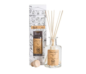 A clear, glass bottle of Milk scented diffuser, with 7 bamboo reeds in the neck of the bottle and a lable printed with " Batons a parfum, fragrance diffuser, lait, milk" and the Lothantique logo. Shown with a second bottle in white packaging with black line drawings of French houses.