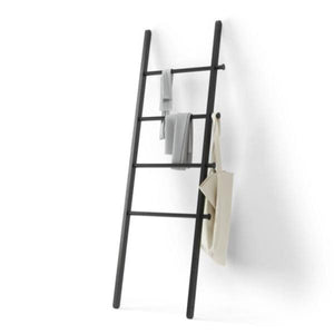 Black ladder with clothes and bags hanging on it on white backdrop